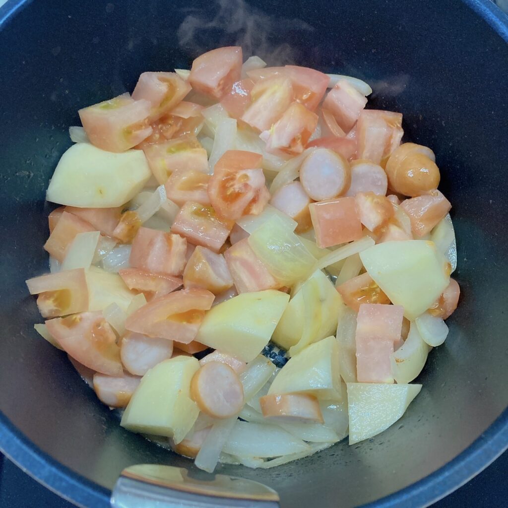 鍋で炒めている玉ねぎ・トマト・ソーセージ・じゃがいも