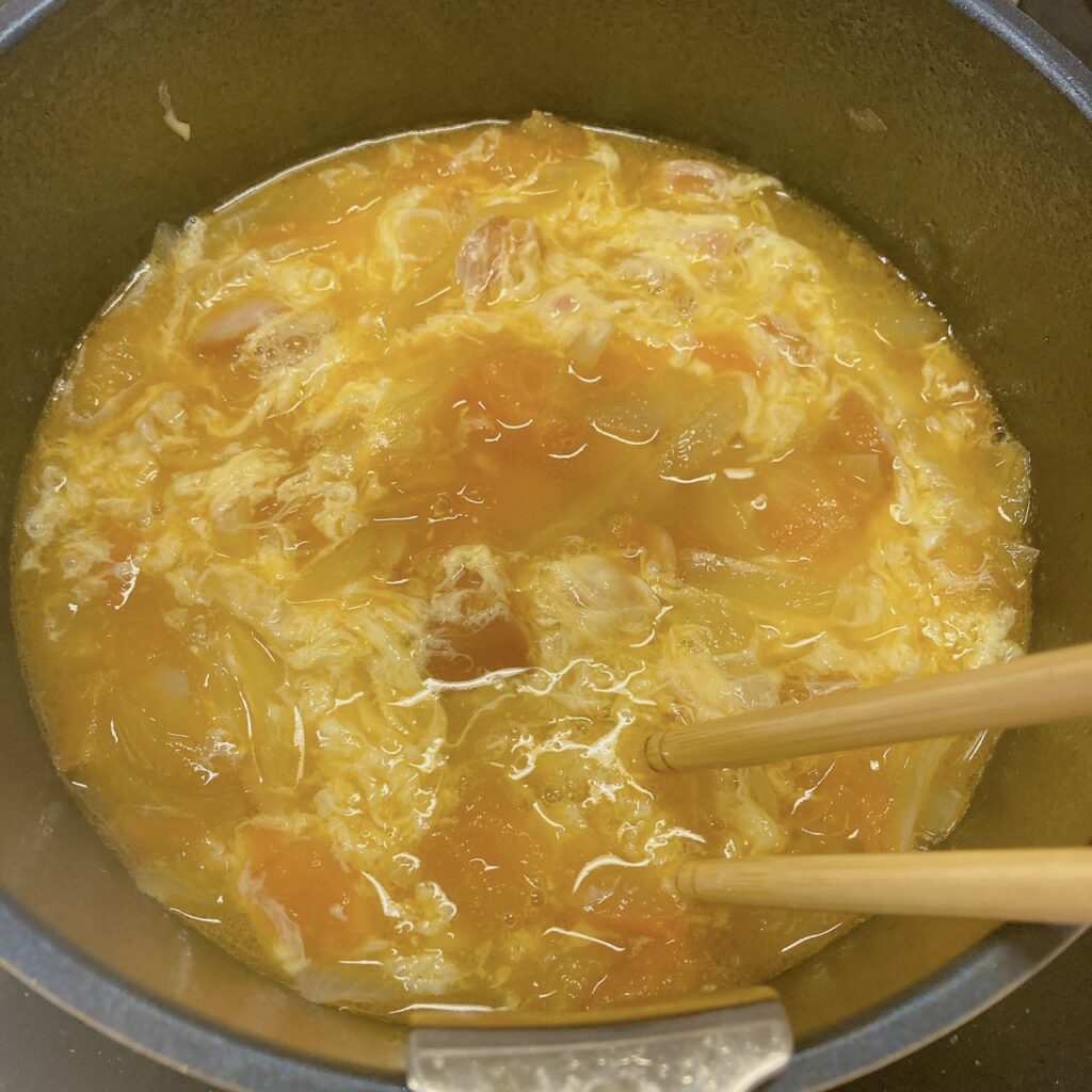 溶き卵を箸で混ぜながらスープを煮ている鍋