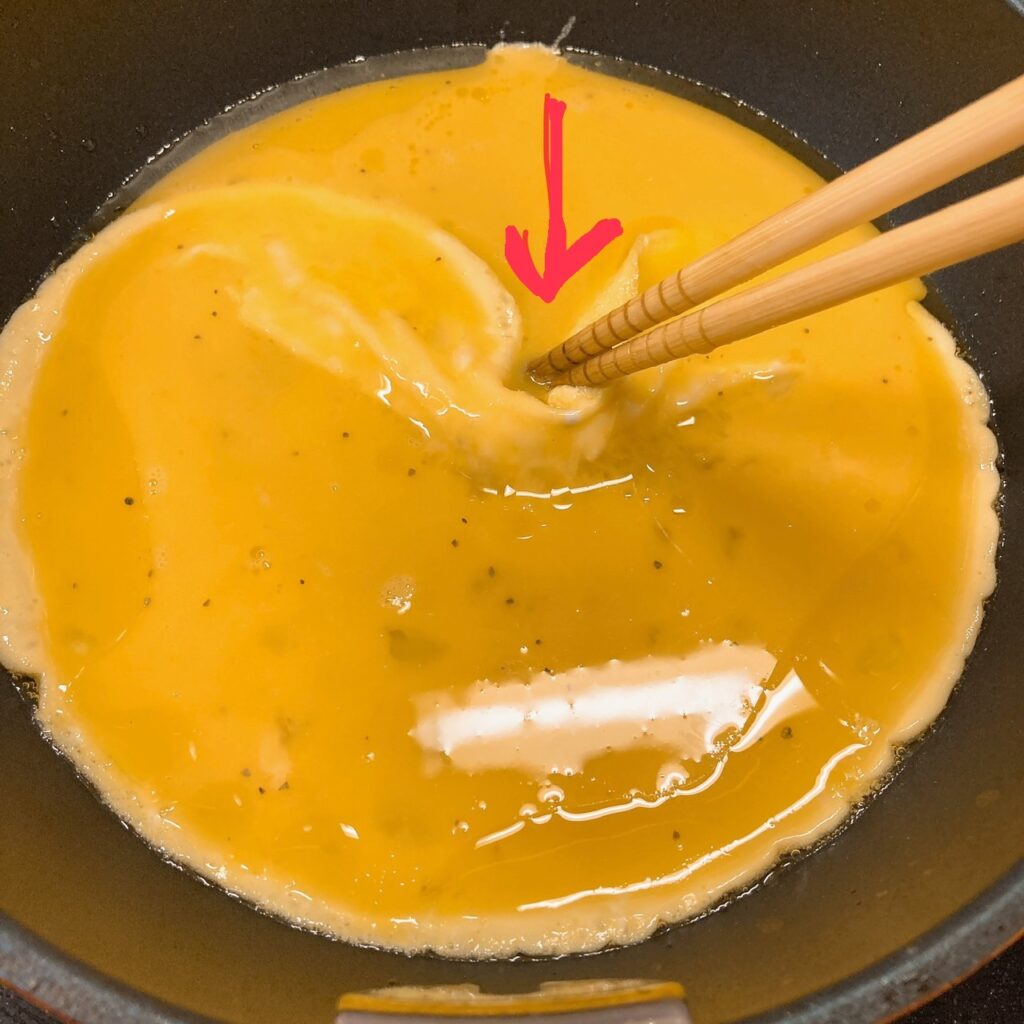 箸で中央に向かって寄せた卵を焼いているフライパン