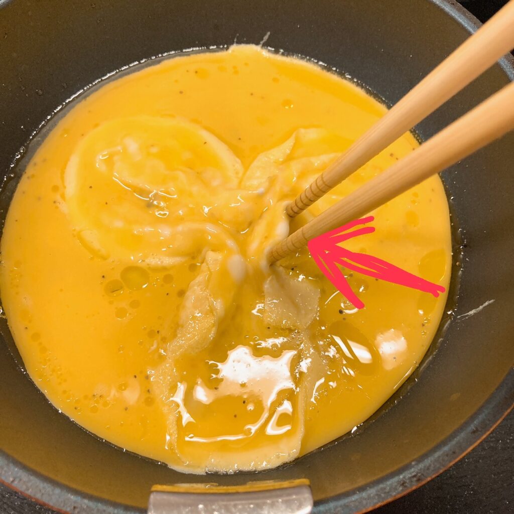 箸で中央に向かって寄せた卵を焼いているフライパン