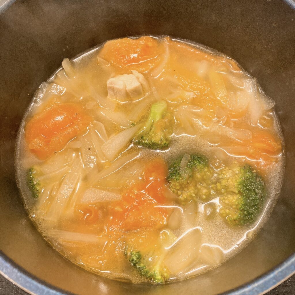水とブロッコリーと玉ねぎとトマトと鶏肉とコンソメスープの素を煮ている鍋
