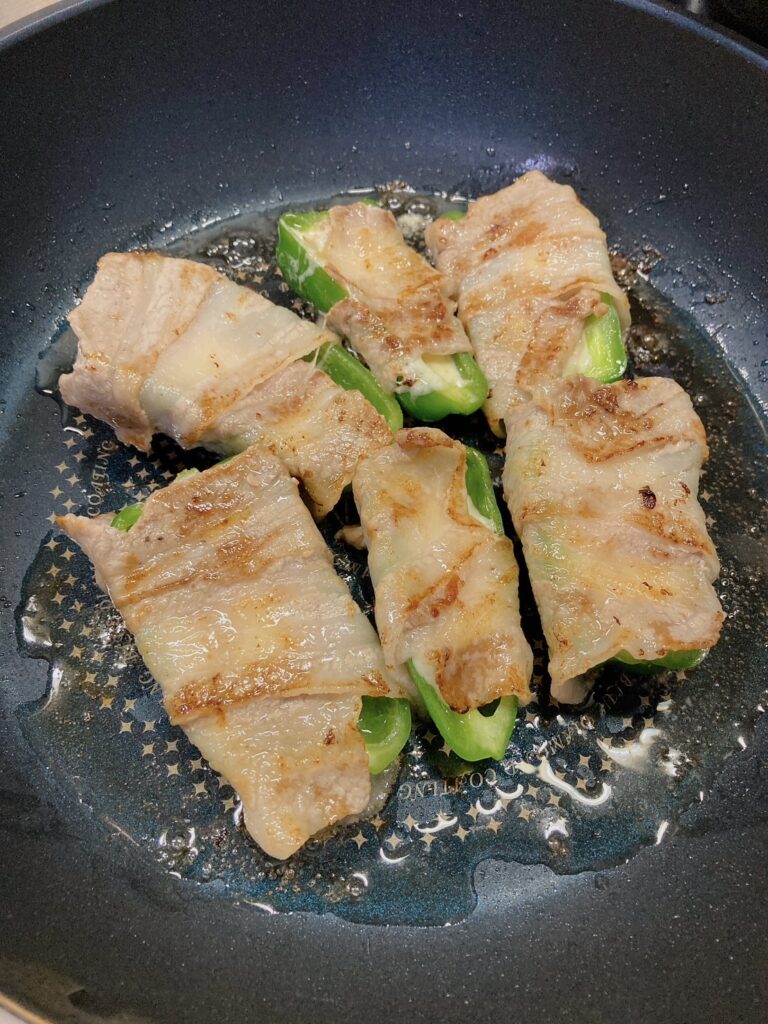 豚バラ肉が巻いてあるチーズ入りのピーマンを焼いているフライパン