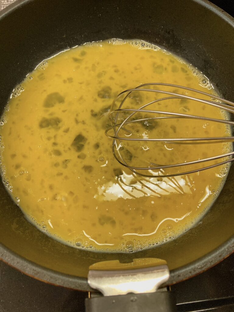 泡だて器で混ぜた卵が入っているフライパン