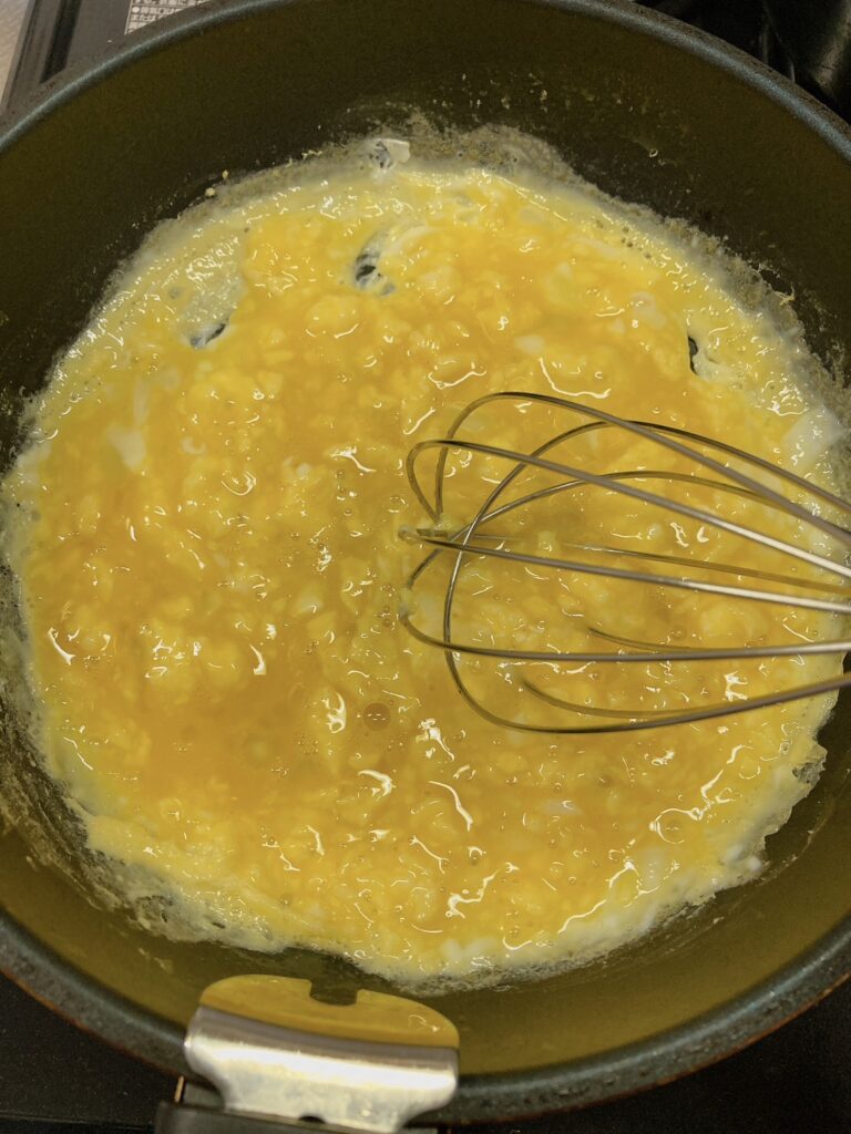 焼きながら泡だて器で混ぜている卵が入っているフライパン