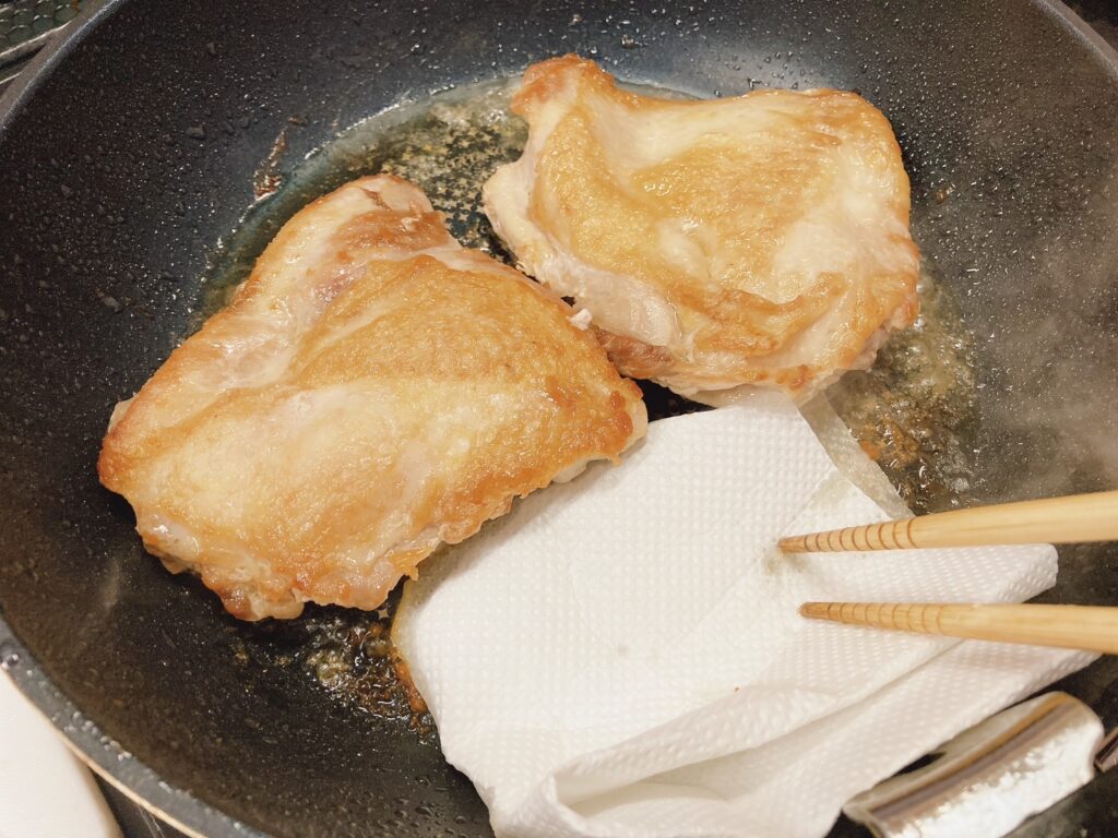 フライパンで焼いている鶏肉から出た肉汁を吸収しているキッチンペーパー