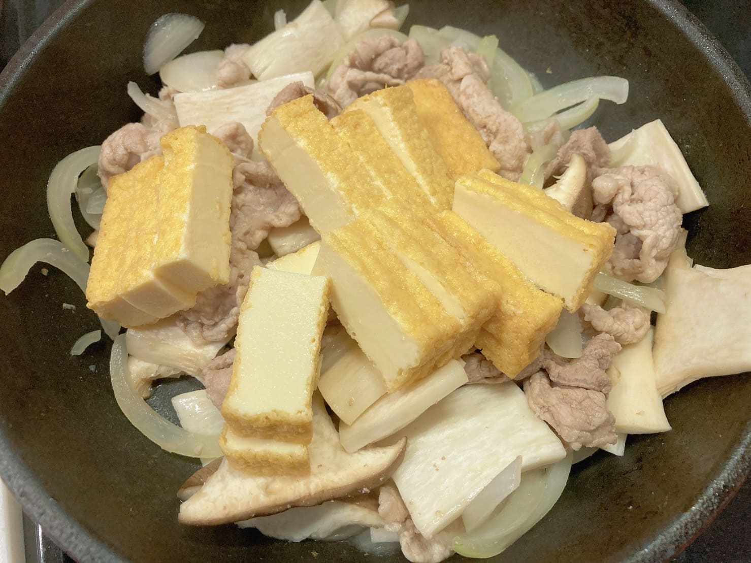 フライパンで炒めている豚肉と玉ねぎとエリンギと厚揚げ